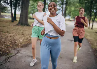 A group of three friends happily running together outside in a park. Learn about intrinsic vs. extrinsic motivation here.