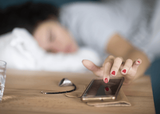 A woman snoozing her alarm on her phone as she lies in bed.