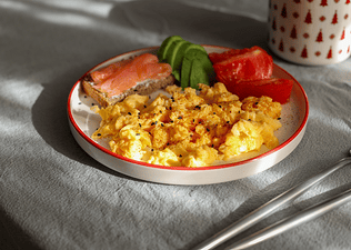A plate with scrambled eggs, avocado, salmon on toast, and tomatoes.