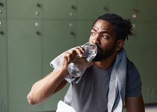 A man drinking water in a gym locker room. He is drinking water to gain muscle.
