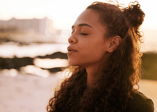 A young woman practicing the box breathing technique outdoors. Her eyes are shut and her face looks calm.