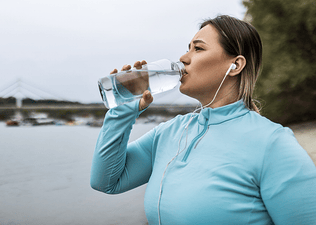 A woman drinking from a clear water bottle during an outdoor workout.
