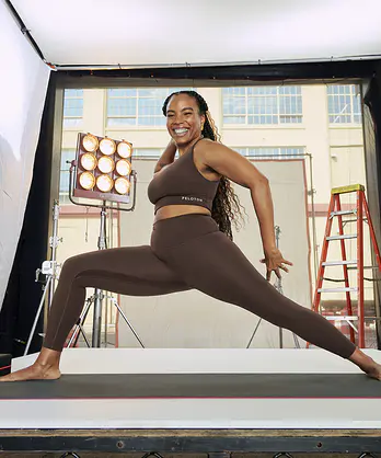 In this image for an article about how gym clothes affect motivation and performance, Peloton instructor Chelsea Jackson Roberts is grinning while doing a forward lunge in a matching brown activewear set.