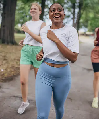 A group of three friends happily running together outside in a park. Learn about intrinsic vs. extrinsic motivation here.