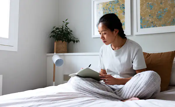 A woman journaling about her goals while sitting on her bed.