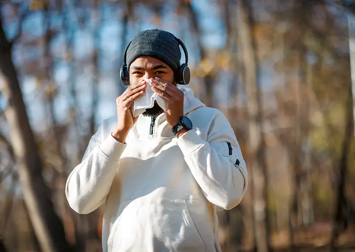 A man going on a run on a chilly day while stopping to blow his nose. He is running while sick.