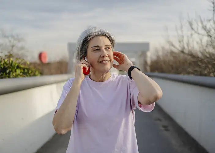 A woman walking outside and listening to music on a warm day. She is exercising to help ease arthritis symptoms.