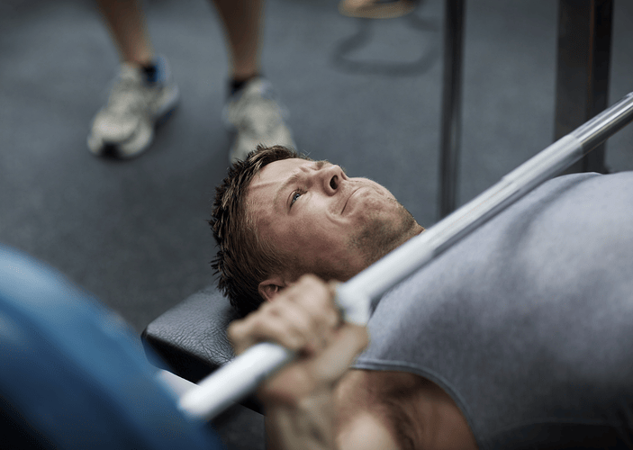 A man about to perform a bench press at the gym with a barbell. He is holding his breath.