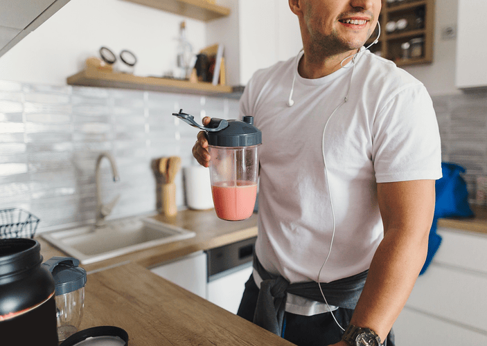 A close-up photo of a man drinking a smoothie in his kitchen, a great post-workout recovery drink.
