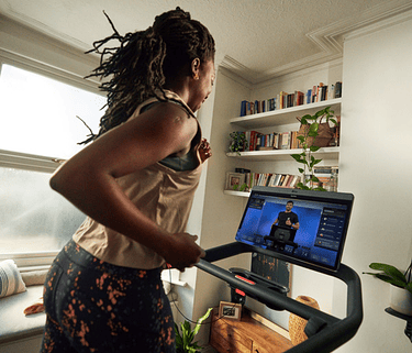 A woman in athletic wear runs on a Peloton Treadmill during a home workout in her apartment
