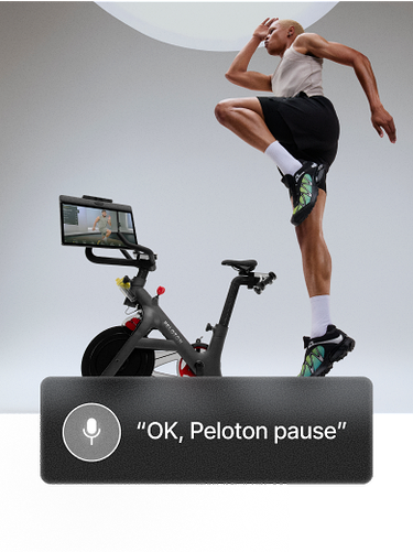 Woman in a light gray tank top and black shorts performs a high knee jump on a mat. Overlay button reads “Pause class.”