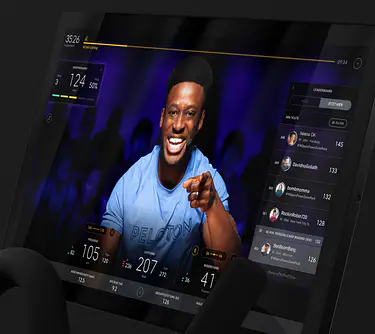Bildschirm des Peloton Bikes mit Peloton-Trainer:in, die/der einen Kurs auf dem Bildschirm unterrichtet. 