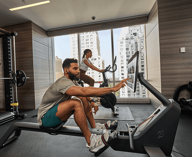 Man on Peloton rower and woman on Peloton bike in hotel gym