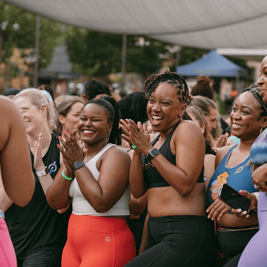 A group of women in workout clothing smiling and clapping as they engage with a Peloton instructor.