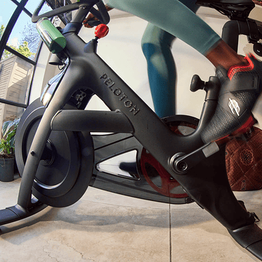 A person rides a Peloton Bike wearing Peloton branded shoes.