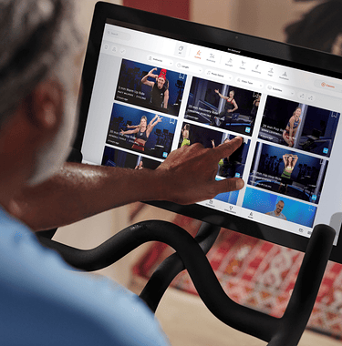 Man on Peloton Bike pointing to classes on Bike touchscreen