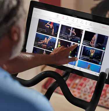 Man on Peloton Bike pointing to classes on Bike touchscreen
