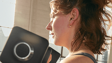 Side profile of a lady in a well lit room curling peloton weights with the Peloton App