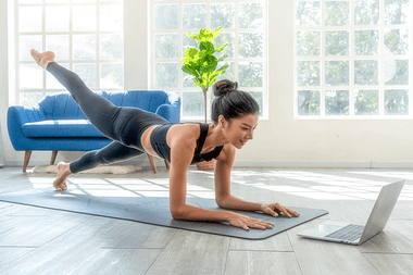 Lady doing yoga on a mat whilst watching a laptop