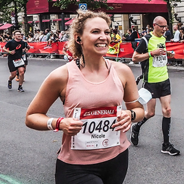 Woman named Nicole wearing a pink tank top and bib number smiling while running a marathon.