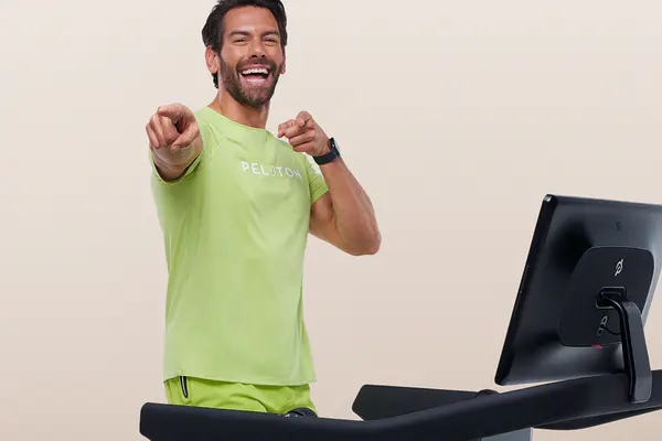 Laughing instructor pointing toward the camera while standing on a Peloton Treadmill.