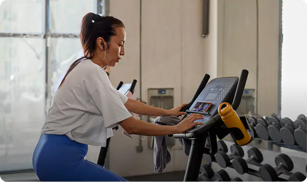 Woman playing a Peloton class on her phone while on a third-party gym bike