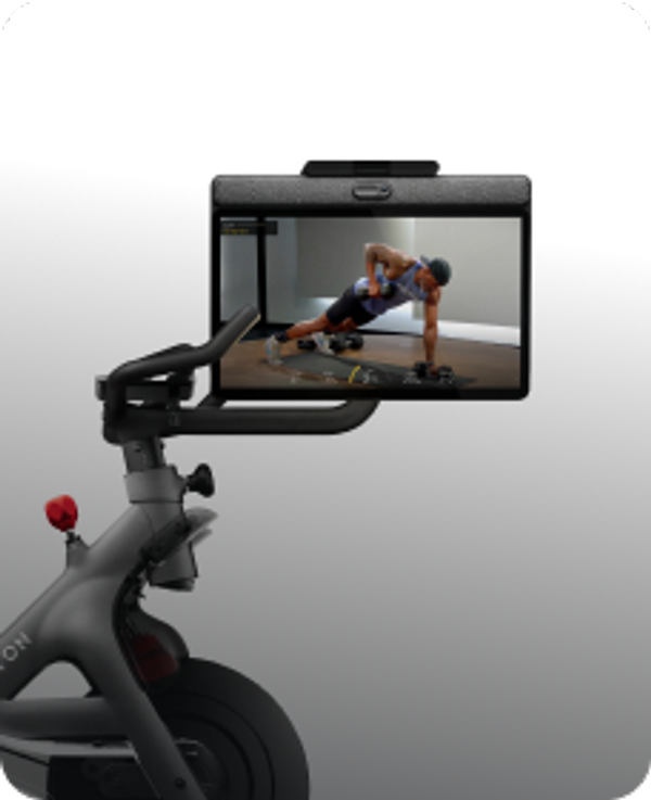 Close-up of a Peloton Bike showing the frame, seat, and handlebars with an attached screen displaying a strength workout class.