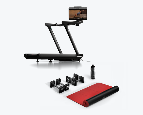 Peloton Tread treadmill displayed alongside two pairs of dumbbells, a water bottle, and a rolled-out exercise mat.