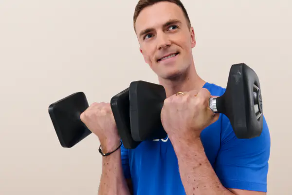 Smiling instructor holding a kettlebell close to her chest during a strength training workout.