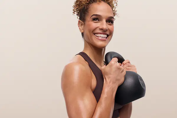 Smiling instructor holding a kettlebell close to her chest during a strength training workout.