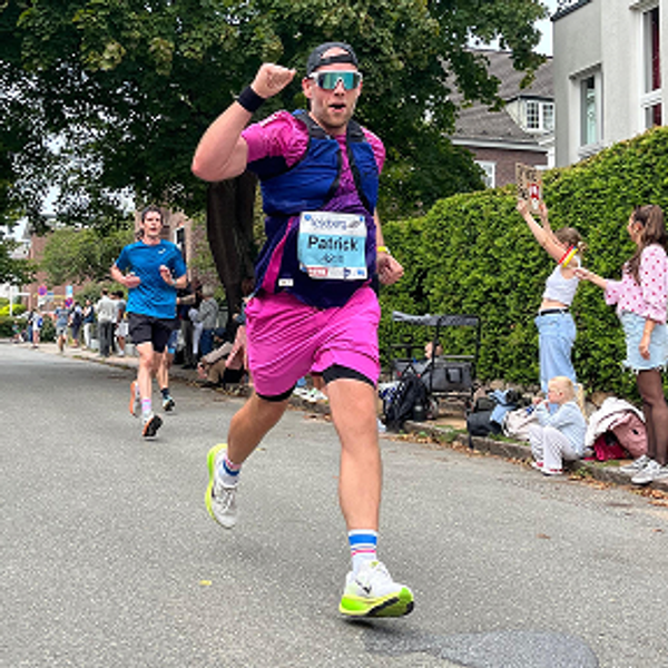 Man named Patrick wearing bright pink shorts and a running vest cheering while running a race.