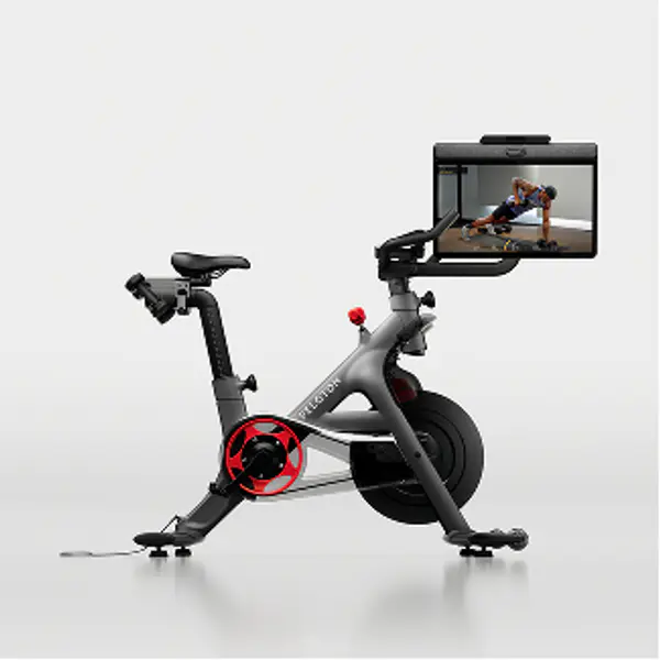 Peloton Bike Plus from the side, featuring an adjustable touchscreen showing a trainer performing a workout.