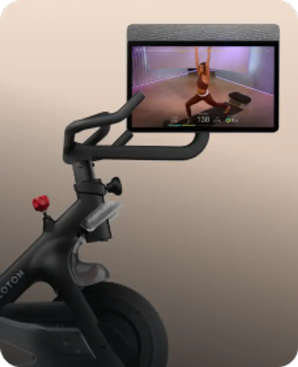 Side profile of a black Peloton Bike with a screen showing a yoga class against a tan background.