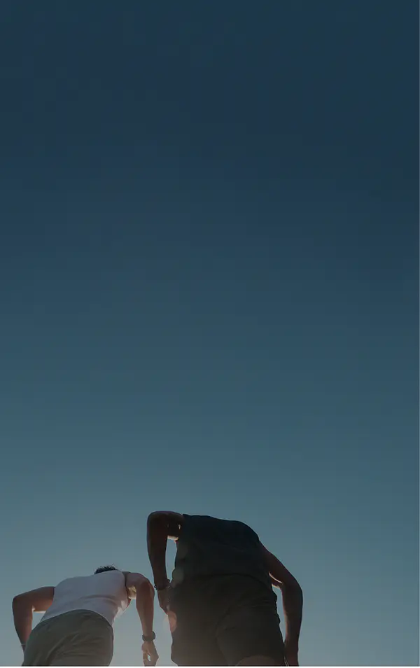 Low-angle view of two runners seen from behind against a bright blue sky.