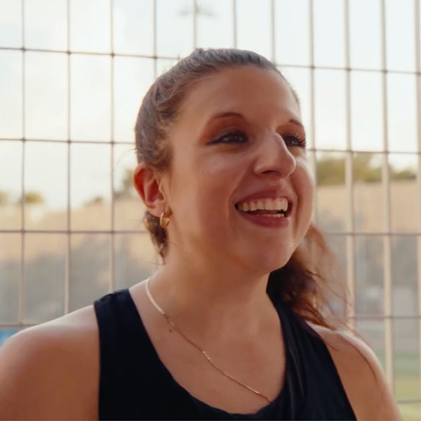 Smiling woman in a black top standing in front of a wire fence outdoors.
