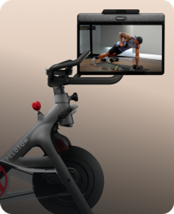 Side profile of a black Peloton Bike+ with a rotating screen showing a strength class against a tan background.