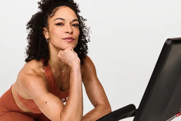 Cycling instructor smiling and leaning against the screen of a Peloton exercise bike.