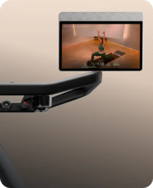 Close-up of a black Peloton Tread handlebar and screen showing a yoga class against a tan background.