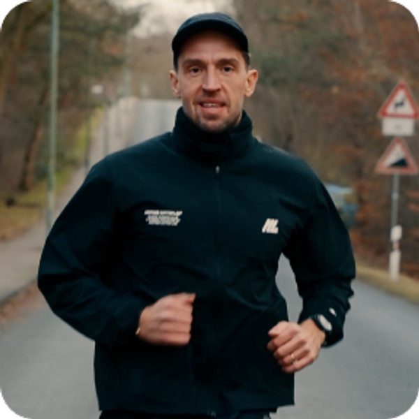 Man wearing a black running jacket and cap running along an outdoor road.