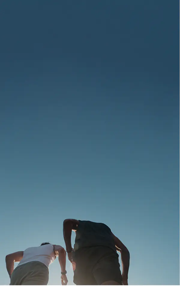 Low-angle view of two runners seen from behind against a bright blue sky.