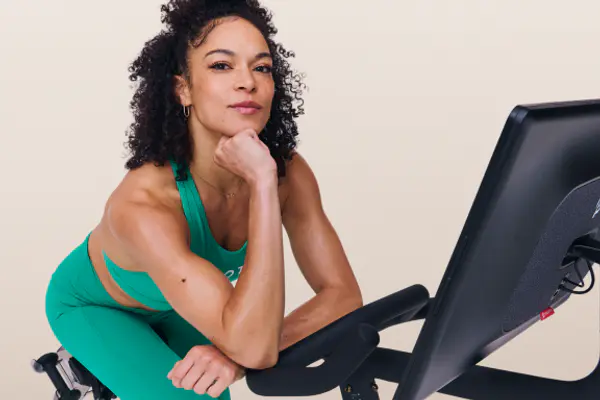 Smiling instructor leaning on the handlebars of a Peloton Bike during a cycling session.