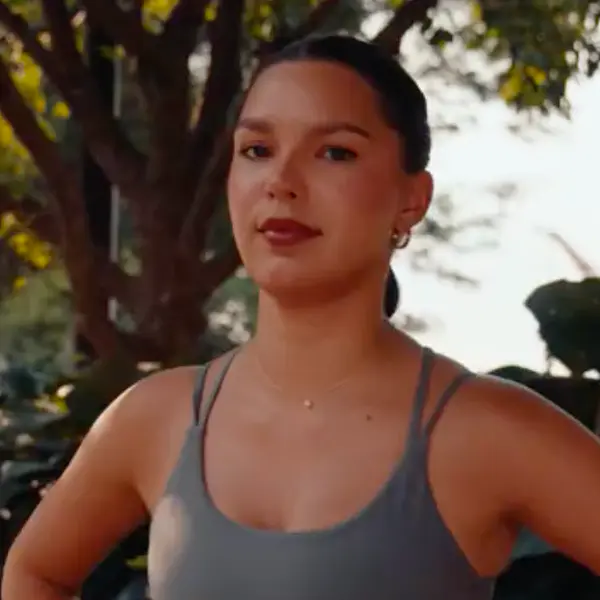 Woman with dark pulled-back hair wearing a grey tank top standing outdoors.