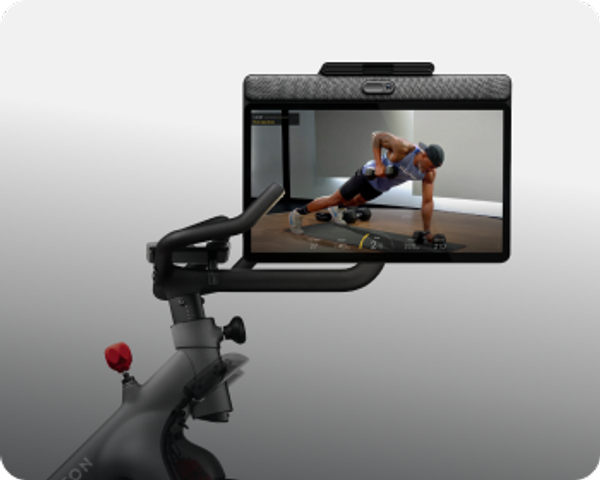 Peloton Bike screen showing an instructor performing a single-arm dumbbell row in a plank position.