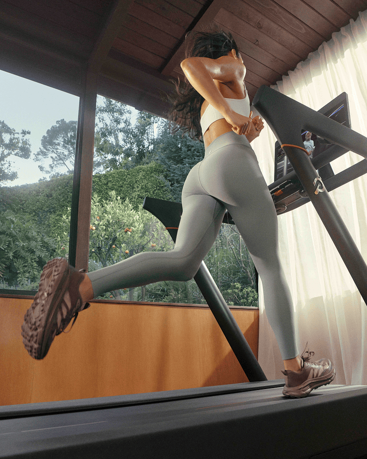 Man running on a sleek modern treadmill inside a bright room with large glass windows.