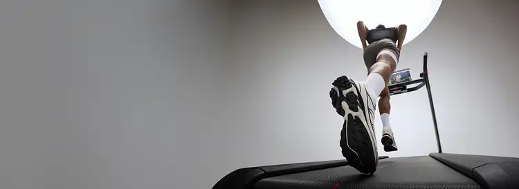 Low-angle view from behind of a man running on a treadmill in a studio setting.
