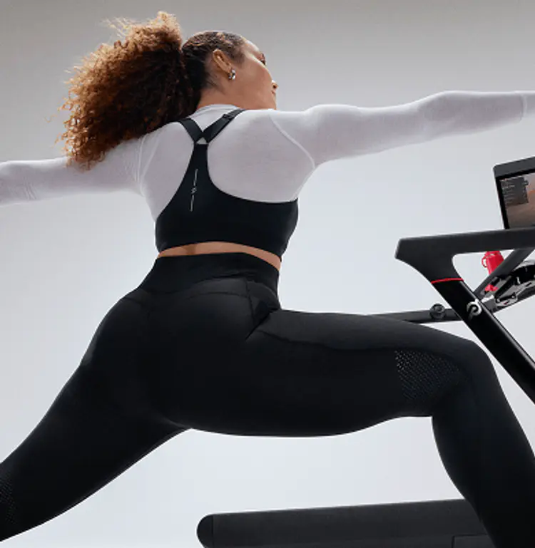 A lady performs stretch beside a Peloton tread whilst following a Peloton class on the Peloton tread swivel screen
