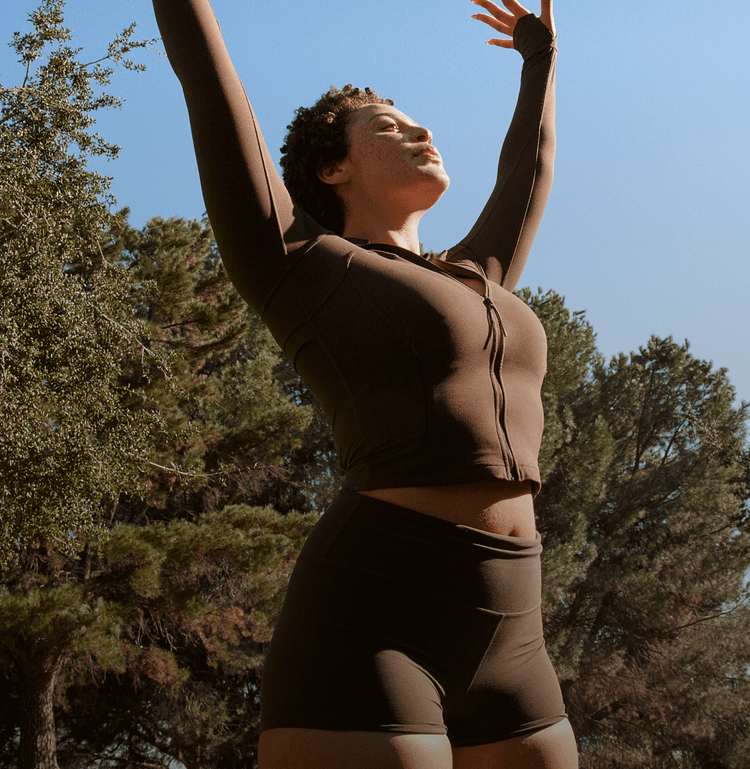 Woman in workout clothes smiling and stretching up outside