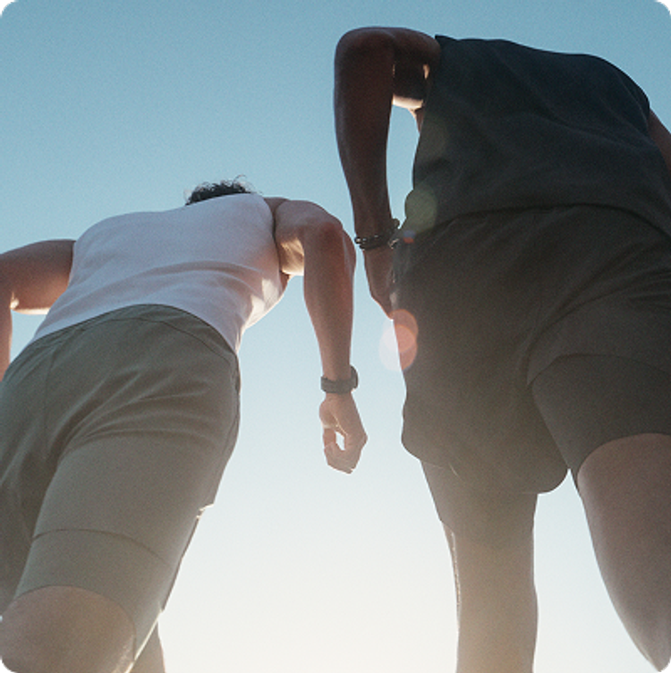Low-angle view of two men running outdoors in athletic tank tops and shorts against a bright blue sky.