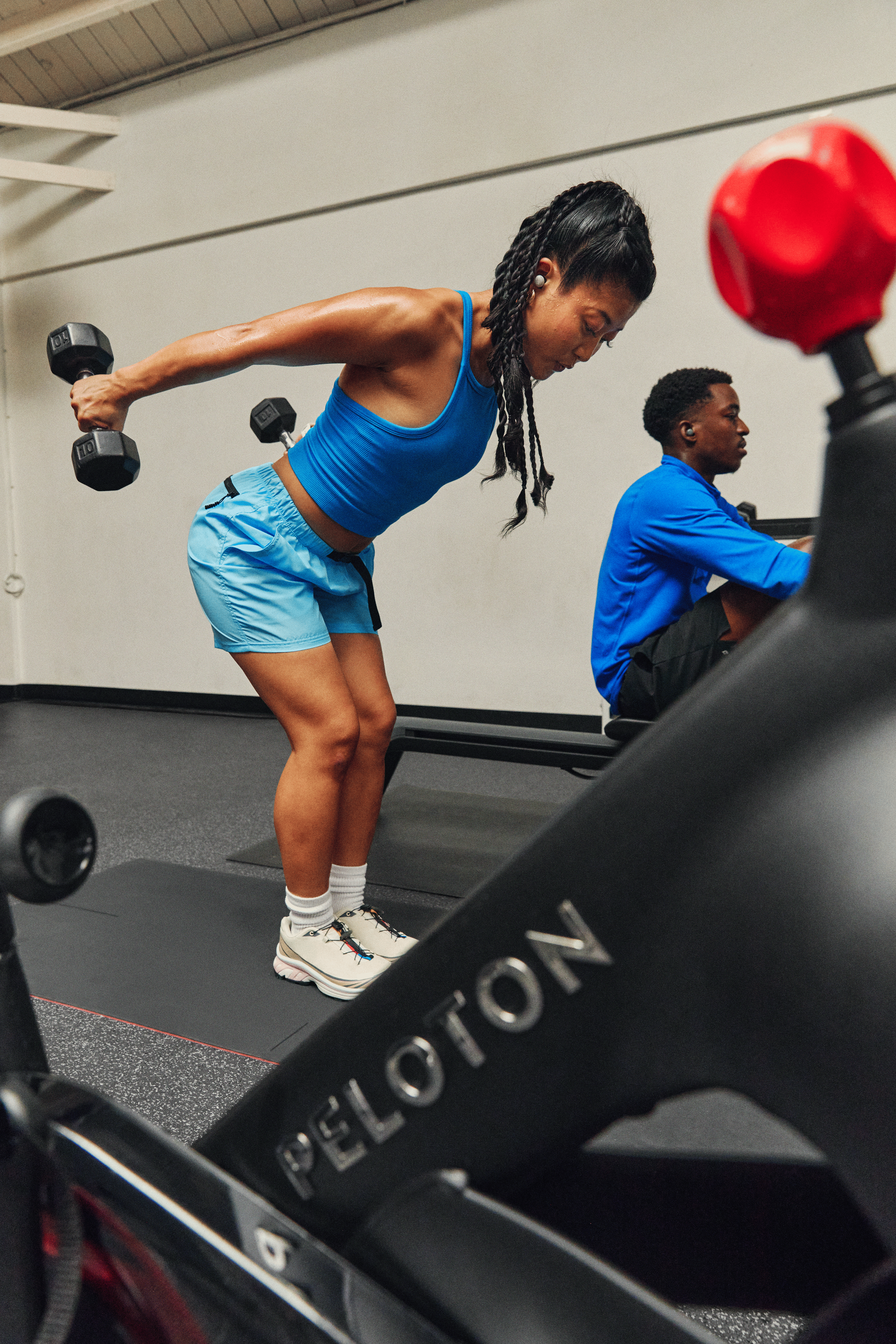 Young woman doing the triceps kickbacks exercise with proper form in a gym next to a Peloton Bike