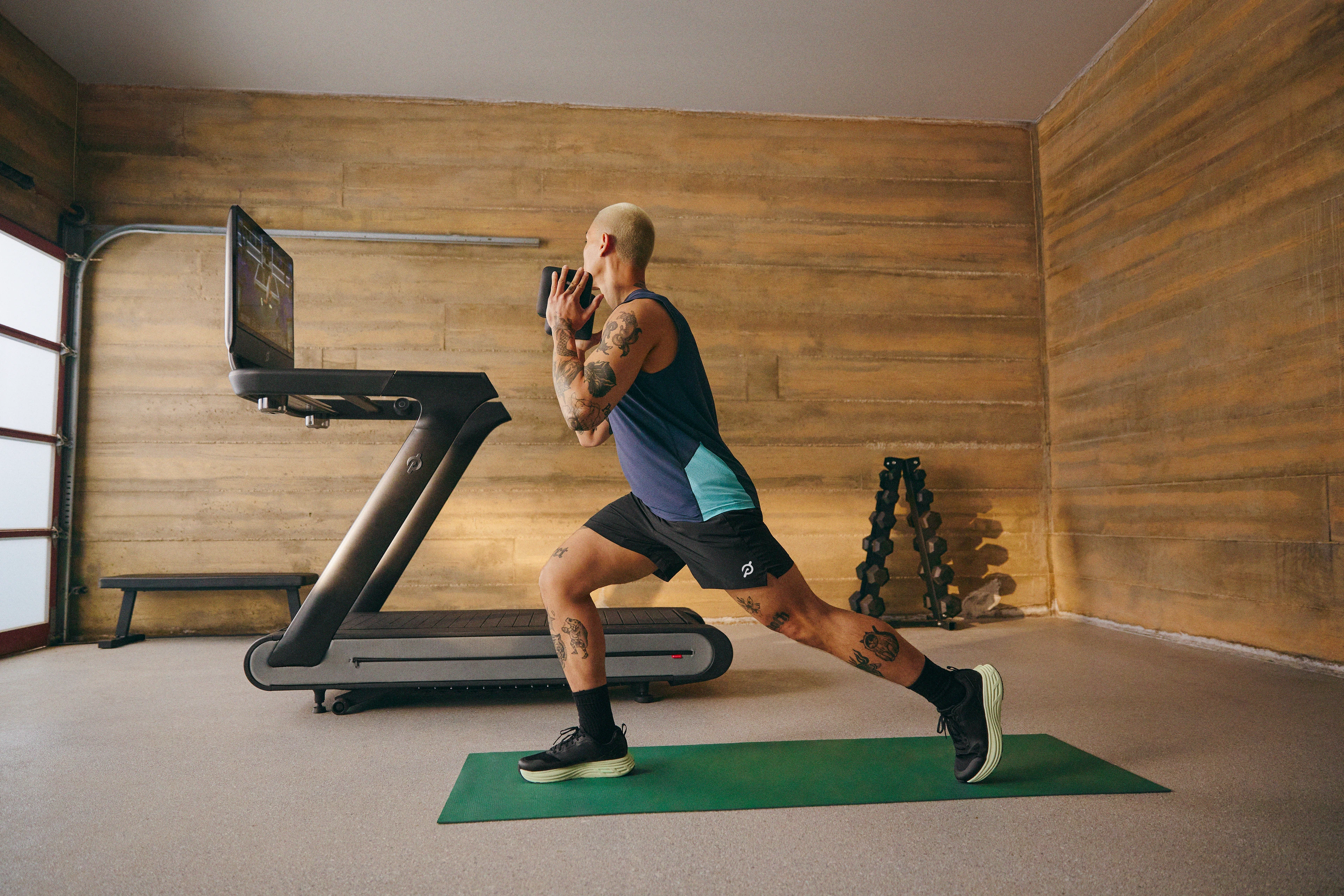 Man doing dumbbell front lunges as part of a quad workout using the Peloton Tread+. 